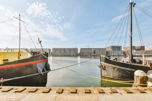 two boats docked at the dock in front of a large building and blue sky with some white clouds above them