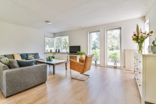 a living room with wood flooring and white walls, including a grey sofa set in the center of the room