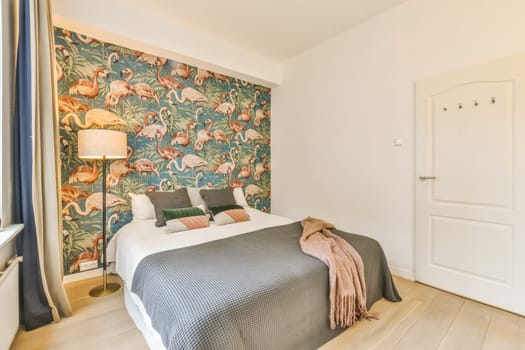 a bed in a room with wallpapers on the walls and wooden flooring, there is a lamp next to the bed