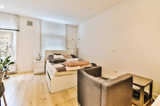a living room with white walls and hardwood flooring, including a small bed in the corner of the room