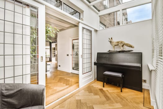 a cat sitting on top of a piano in a living room with wood flooring and white brick wall behind it