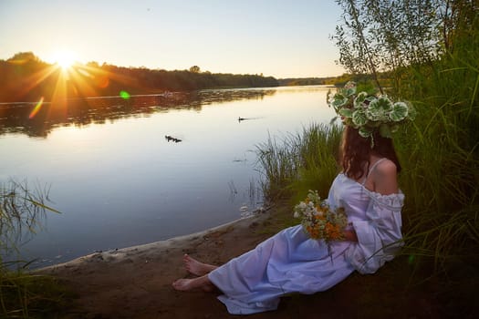Slavic plump chubby girl in long white dress on the feast of Ivan Kupala with flowers and water in a river or lake on summer evening