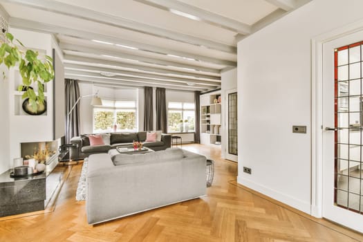 a living room with wood flooring and white walls in the center of the room is a grey couch, coffee table, mirror