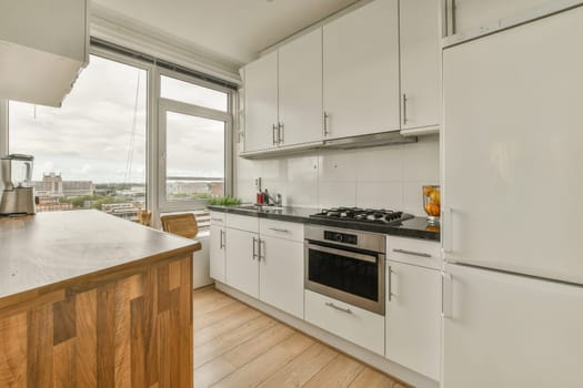 a kitchen with wood flooring and white cupboards on either side, looking out to the city from an open window