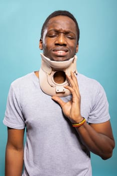 Distressed young man wearing a cervical collar to heal from an injury. Portrait of a male individual with a neck support, enduring pain from fractured vertebrae during recovery.