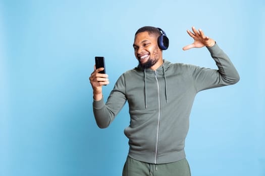 African american upbeat adult changing the song on his smartphone, having fun with his favorite funky music on headphones. Carefree confident young guy dancing around in studio.