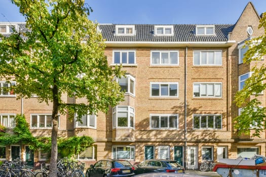 an apartment complex in the netherlands, with bikes parked on the street and cars parked along the curbed road