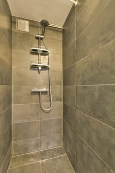a shower room with tile walls and grey tiles on the wall, there is a hand held shower in the corner