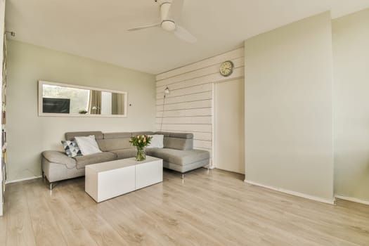 a living room with wood flooring and white paint on the walls, ceiling fan is mounted above the couch