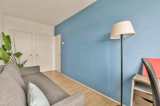 a living room with blue walls and hardwood flooring, including a grey couch in front of a white door