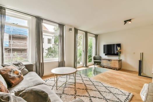 a living room with hardwood flooring and large windows looking out onto the garden outside, there is a tv set in the corner