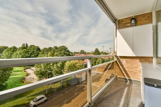 a balcony with a view of the trees and buildings in the distance, taken from an apartment window looking out onto the street