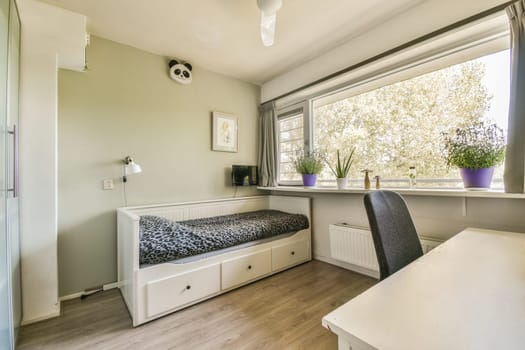 a small room with a desk and some plants in the window simh is on the wall next to the bed