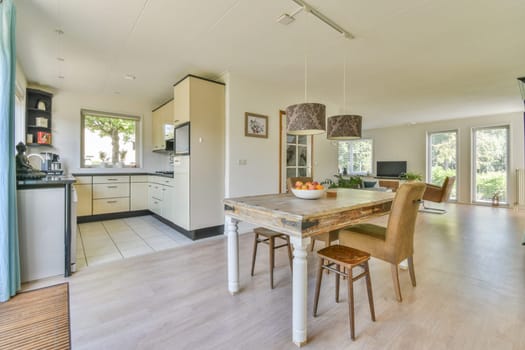 a kitchen and dining area in a house with wood flooring, white walls, wooden floors, and large windows