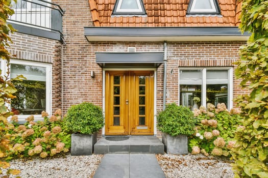 the front entrance to a house with plants and flowers in pots on either sides, surrounded by red brick walls
