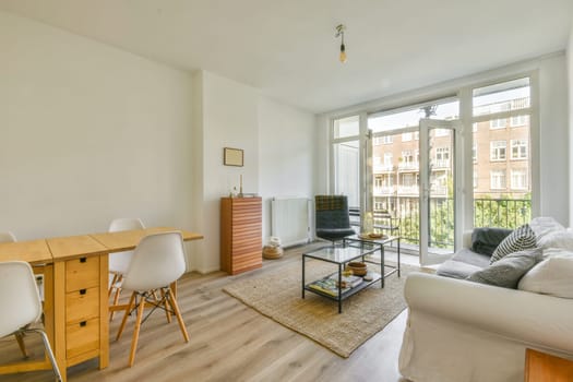 a living room with wood flooring and white walls, there is a small dining table in front of the couch