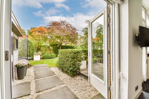 the outside of a house from inside an open door looking out onto a garden with trees and bushes in the background
