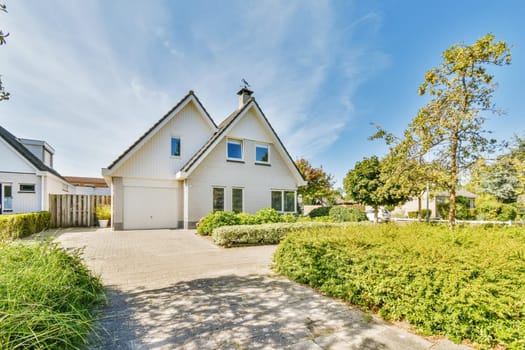 a house with white sidings and blue sky in the background there is a driveway leading up to the front door