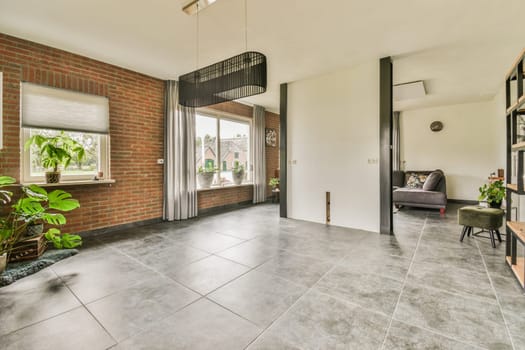 a living room with red brick walls and grey tile flooring in the center of the room is an open door that leads to a patio