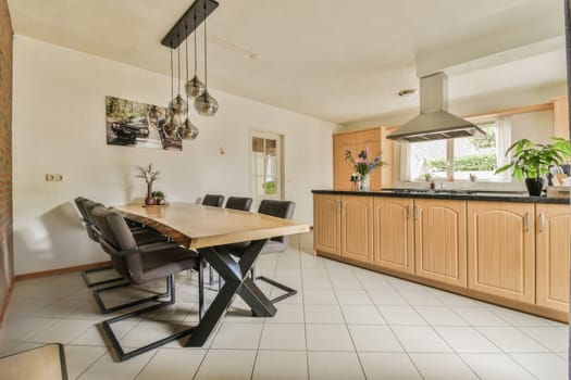 a kitchen and dining area in a house with white tiles on the floor, wooden cabinetry, and black chairs