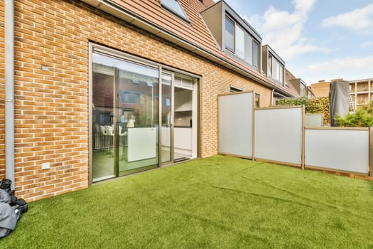 an outside area with green grass and brick buildings in the background, including a sliding glass door that leads to a patio