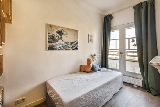 a cat sitting on a bed in a small room with a painting hanging above the bed and an open window
