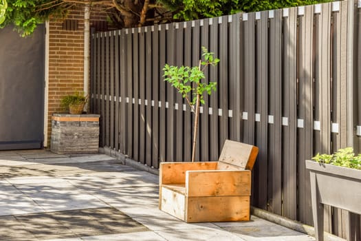 a small tree growing in a box on the sidewalk next to a wooden fence that has been painted with white paint