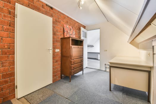 a room with a brick wall and an open white door in the center of the room is a small desk