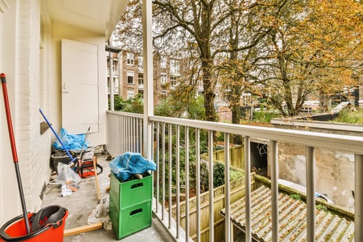 a balcony with trash bins and mops on the floor next to an open door, in front of a tree