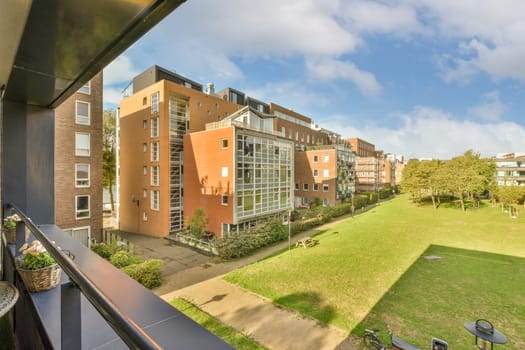 an outside area with some buildings and green grass in the photo is taken from a balcony looking out onto the street
