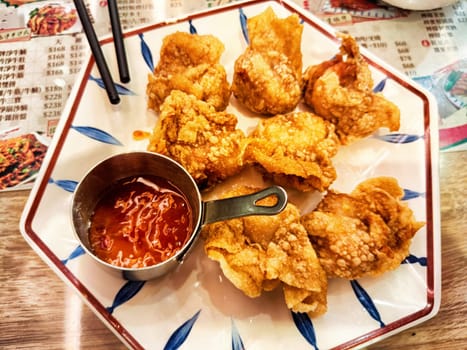 Golden brown crispy dumplings arranged on a decorative plate with a flavorful spicy dipping sauce nearby, enjoyed in a lively dining atmosphere.