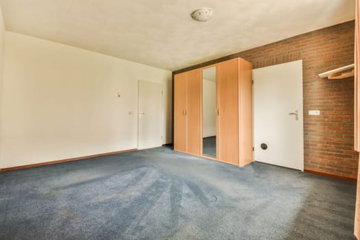 an empty room with blue carpet and red brick wall in the background, there is a door to another room