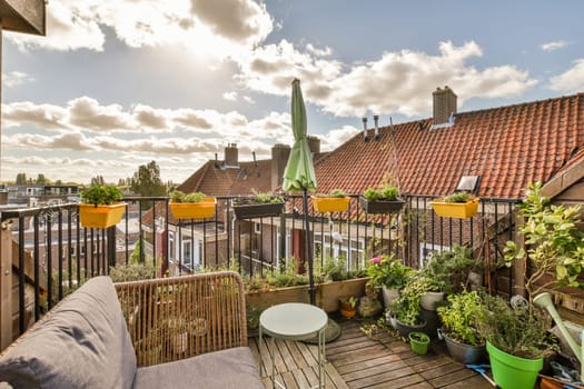 a balcony with plants and pots on the railing, in front of a house that has red tiled roofs