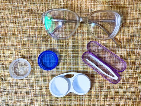 Eyewear and contact lens items are neatly placed on a textured fabric, showcasing tools for maintaining visual clarity and comfort.