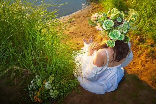 Slavic plump chubby girl in long white dress on the feast of Ivan Kupala with flowers and water in a river or lake on summer evening
