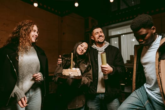Group of four friends enjoy a cozy evening indoors, celebrating with a cake. They share laughter and joy as they pose together in warm, inviting light.