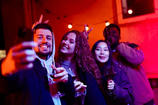 Group of friends celebrating at a lively party in an urban area, holding wine glasses and posing cheerfully under colorful lights in the evening.