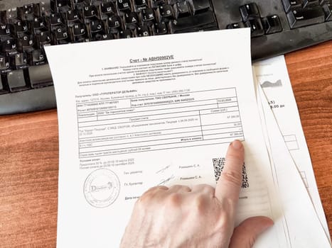 Kirov, Russia - March 18, 2025: A hand points at a payment receipt on a cluttered desk next to a computer keyboard, indicating financial transactions.