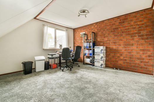 a room with a brick wall and an office chair in the corner, next to a computer on a desk