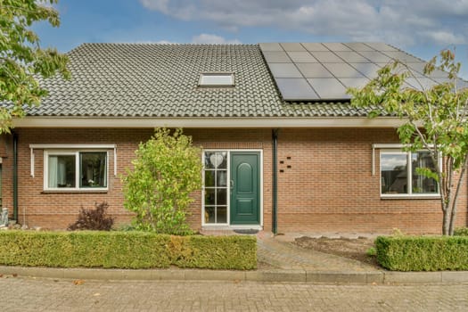 a brick house with solar panels on the roof and green plants growing in the front yard next to the door