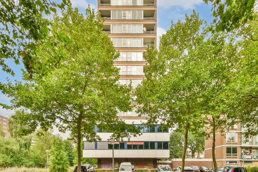 some cars parked in front of an apartment building with trees on the side and blue sky above it, as seen from the street