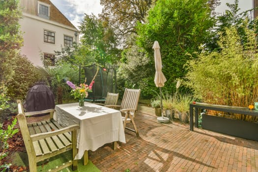 a patio with chairs, tables and umbrellas on the table in front of a house surrounded by lush green trees