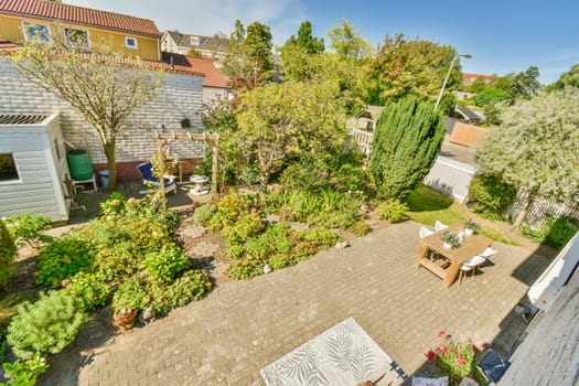 a backyard area with lots of plants and flowers on the ground, including an umbrella, table, chairs, and other items