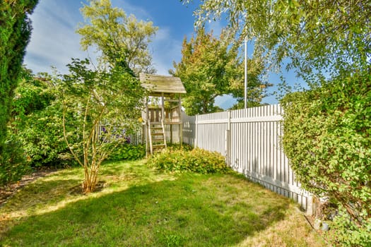 a white fenced yard with trees and bushes in the foreground area on a bright sunny day photo taken from above