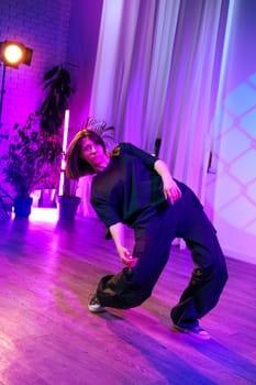 A dancer showcases expressive movements in a stylish studio space illuminated by vibrant purple and pink lights. The setting emphasizes creativity and artistic flair during the evening.