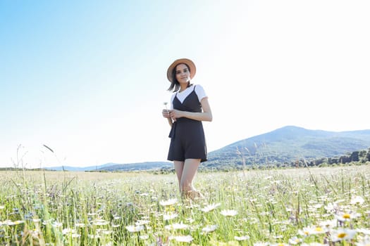 Beautiful woman in dress walking with flowers in a field of daisies
