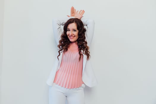 brunette woman showing her hands the ears of a hare on the white background of the office