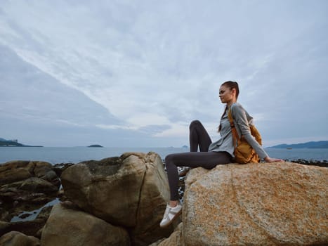 A young woman in casual outdoor clothing sits on a rock by the sea, gazing at the horizon The scene evokes a sense of peace, adventure, and connection with nature