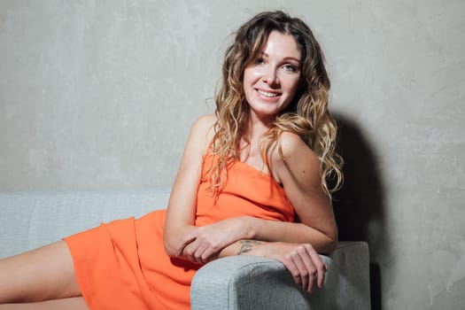 Beautiful woman smiling in orange dress on sofa