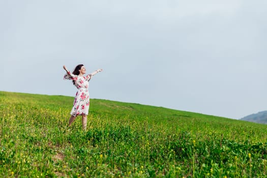 brunette woman standing with her arms outstretched in a field of flowers in spring and smiling